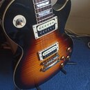 Elektrická kytara s tmelelovým korpusem v barevné gradaci od černé přes červenou po žlutou. Nástroj má dva humbuckery s krémovými rámečky a čtyři zla…