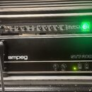 V hliníkovém racku jsou umístěna dvě černá zařízení značky Ampeg. Horní jednotka nese nápis SVPCL ALL TUBE BASS PREAMP a má vpravo svítící zelený kru…