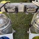 Dvě stříbrné kovové reflektory umístěné na vodorovném hliníkovém profilu. Na profilu jsou dva černé vícepinové konektory a bílý štítek s nápisy: „Occ…