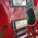 Detail červené elektrické kytary s černým pickguardem. Nástroj má dva snímače s kovovými kryty a chromovaný kobylník s Tune-o-matic systémem. Povrch…