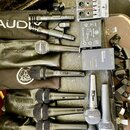 Sestava mikrofonů a příslušenství na černém povrchu. Jsou zde mikrofony značek AUDIX, SHURE, AKG s nápisem PERCEPTION 220 a RØDE MICROPHONES. K dispo…
