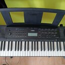 Černý digitální klavír s bílými a černými klávesami. Na ovládacím panelu je logo YAMAHA a modelové označení PSR-223. V horní části je umístěn černý p…