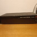 Černý rackový stereo výkonový zesilovač s kovovým šasi a ventilačními otvory na horní straně. Na předním panelu je bílý nápis STEREO POWER AMPLIFIER…