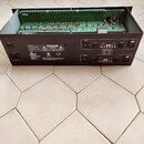 Černý rackový procesor s otevřeným šasi, ve kterém je viditelná zelená základní deska s elektronickými součástkami. Na zadním panelu jsou nápisy „dbx…