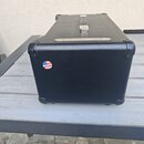 Černý kytarový kombozesilovač s povrchem z imitace kůže a kovými rohy. Na zadní straně je nalepená kulatá nálepka s vlajkou USA a nápisem Proudly Mad…