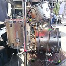 Stříbrná bicí souprava s glitrovým povrchem. Na tomu a basovém bubnu je viditelné logo "Gretsch". Souprava zahrnuje tom, basový buben a činely na chr…