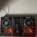 Černý DJ kontrolér značky Numark s označením PARTY MIX. Zařízení má dvě stříbrné jog-kola, centrální mixážní sekci s knoflíky a dvě sady červených po…
