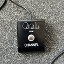 Černý kovový nožní spínač s připojeným kabelem. Na horní straně je bílé logo Paul Reed Smith, pod ním označení FS1M a ve spodní části nápis CHANNEL.…