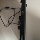 Černý plastový kontrolér ve tvaru kytary s připojeným USB kabelem. Na boku je vidět bílý nápis "PLAYSTATION 3" a část loga "Rock". Povrch je v dobrém…
