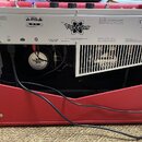 Zadní strana červeného kytarového komba s nápisem MODEL Vaporizer. Na zadním panelu jsou vidět loga CE, G-Mark a UL, nápis FENDER MUSICAL INSTRUMENTS…