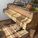 Dřevěný piano v přirozené barvě dřeva s viditnou masivní strukturou. Nástroj má zdobený notový pult a robustní tocené nohy. Povrch vykazuje známky op…
