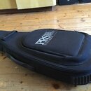 Černý polotvrdý pouzdro na kytaru z textilního materiálu. Na horní části je bílý nápis PRS PAUL REED SMITH GUITARS. Pouzdro vykazuje mírné známky pou…