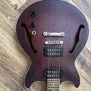Tmavě hnědá polodublá elektrická kytara s dvěma f-otvory a dvěma černými humbuckery. Nástroj má dva černé oválné knofíky a chromovaný most s kladeným…