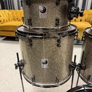 Dvě stohované bicí bubny s povrchem v šedé glitrové barvě a chromovaným kováním. Na obou bubnech je čtvercový štítek s logem a nápisem Jelen DRUMS. V…