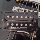Černý humbucker s dvěma řadami snímacích pólů, umístěný v černém plastovém rámečku na černé kytare. Na spodní části snímače je bílý nápis Seymour Dun…