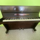 Tmavě hnědé digitální piano s otevřeným víkem. Nad klávesnicí je umístěn nápis „Hofmann & Cerny“. Nástroj stojí na dvou nohách a má dvě pedály. Povrc…