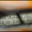 Detailní pohled na štítek uvnitř hudebního nástroje. Na štítku je černý nápis: „Pietro Antonio dalla Costa fece in Treviso Anno 17“. Papír štítku je…