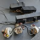 Tři černé elektrické snímače kytary v různých velikostech, dva menší a jeden dlouhý. K nim jsou připojeny tři bílé potenciometry s připojeným zapojov…