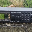 Černý rackový procesor s nápisy FRACTAL AUDIO SYSTEMS a Axe-Fx II PREAMP/FX PROCESSOR. Zařízení má displej, několik tlačítek s popisky jako LAYOUT, G…