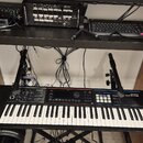 Na fotce je černý klávesový syntezátor s bílými a černými klávesami, na kterém je nápis Roland JUNO-DS. Nástroj je umístěn na černém stojanu, v jehož…