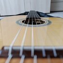 Akustická kytara s přírodním povrchem desky a tmavým hmatníkem. Kolem otvoru rezonančního otvoru je viditelný dekorativní lem. Vnitřní část otvoru ob…