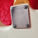 Detail krku a těla bílé elektrické kytary. Na dřevěném krku je nápis MADE IN JAPAN a pod ním nečitelný kód. Kovová krytka hрифu je přišroubovaná čtyř…