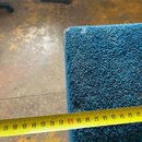 Detailní záběr na roh modrého, texturovaného předmětu z materiálu připomínajícího kobercovinu nebo plst. Kolem předmětu je přiloženo žlutév metr, kte…