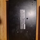 Spodní strana černého elektronického zařízení v plastovém provedení. Na bílém štítku je uveden nápis MODEL: SL26, značka KORG a označení MADE IN JAPA…