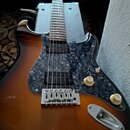 Elektrická kytara s trupem v barevném přechodu od tmavě hnědé k žluté. Nástroj má tmavý vzorovaný pickguard, tři snímače a dva bílé oválné knofíky s…