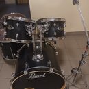 Černá bicí souprava s chromovaným kováním. Na basovém bubně je bílý nápis Pearl, na tom-tamech jsou viditelné oválné loga Pearl. Souprava obsahuje ba…