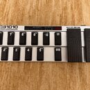 Stříbrný MIDI pedál s černými spínači a dvěma expresními pedály. Na levé straně je nápis FCB1010 MIDI FOOT CONTROLLER a nad spínači jsou sekce PRESET…