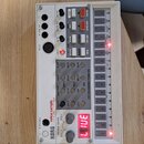 Bílý sampler s názvy KORG a volca sample DIGITAL SAMPLE LESS SEQUENCER. Zařízení obsahuje řadu posuvníků, tlačítek a červeně svítící displej s nápise…