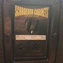 Detail zadní strany reproduktorové skříně s černým povrchem. Na horním štítku je žlutý nápis SCHROEDER CABINETS a pod ním menší text SUPERIOR SOUND.…