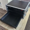 Černý transportní flightcase s hliníkovými hranami a vrškem. V horním slotu je osazen černý přístroj s nápisy "Trakker" a "T-100", který obsahuje řad…