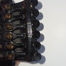 Detailní pohled na černý kytarový kobylník s šesti ladicími šrouby. Na boku je umístěn stříbrný nápis "Ibanez". Povrch vykazuje známky opotřebení a d…