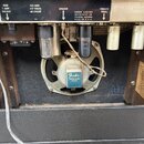 Fotografie zachycuje vnitřek kytarového komba s viditelným reproduktorem a elektronickými komponenty. Na horním bílém panelu jsou nápisy FUSE 1 AMP.…