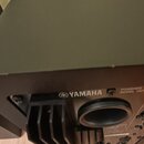 Detail zadní strany černého aktivního reproduktoru. Na šasi je bílý nápis YAMAHA s logem značky a text POWERED SPEAKER SYSTEM MODEL HSP. Jsou vidět c…