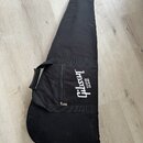 Černý textilní obal na kytaru s rukojetí a ramenním popruhem. Na boku je bílý nápis Gibson USA. Povrch materiálu vykazuje lehké znečištění a opotřebe…