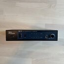 Černý rackový vysílač s nápisy „the L.T.bone“ a „IEM-75T UHF STEREO WIRELESS PLL TRANSMITTER“. Přístroj má digitální displej, dva LED indikátory úrov…
