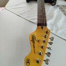 Elektrická kytara s hnědým gradientem těla a světlým dřevěným krčkem. Na hlavě je nápis „Vintage ICON Series™“ a v dolní části logo „V6“. Nástroj vyk…