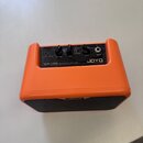 Oranžový kombozesilovač s černým ovládacím panelem a černou přední mřížkou reproduktoru. Na panelu jsou nápisy JOYO, MA-10A ACOUSTIC GUITAR a popisky…