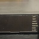 Černý výkonový zesilovač značky BOSE. Na pravé straně je bílý nápis PowerShareX Adaptable Power Amplifier a vlevo označení PSX1204D. Uprostřed se nac…