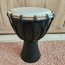 Černý djembe s hrací plochou z pleti v přirozené světlé barvě. Horní okraj je opleten kombinací černého a béžového provázku. Na těle nástroje nejsou…