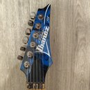 Detail hlavy elektrické kytary v modré barvě s černým grafickým vzorem. Na hlavě je bílý nápis Ibanez, nad ním slovo Premium a vpravo nápis JEM. Kyta…