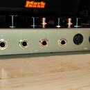 Zadní strana stříbrného elektronického zařízení s řadou ovládacích knoflíků na horní ploše. Jsou zde viditelné konektory s popisky L/MIC INPUT, R a L…