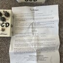 Fotografie zobrazuje efekt pedál v krabičce s přiloženým manuálem. Na pedálu je bílý povrch a nápisy Fulltone OCD OVERDRIVE/DISTORTION. V horní části…