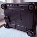 Fotografie zachycuje spodní stranu černého elektronického zařízení z plastu. Jsou vidět čtyři kulaté nožičky a několik ventilačních mřížek. V dolní č…