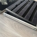Fotografie ukazuje otevřený transportní kufr s hliníkovým profilem a kovovými rohy. Vnitřní prostor obsahuje černou vložku s několika polstrovanými p…