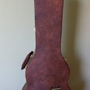 Hnědý tvrdý kufýr na kytaru s texturovaným povrchem. V dolní části je umístěno žluté logo Gibson. Kufýr má kovové zapínání a kožený úchyt.