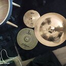 Tři mosazné činely různých velikostí položené na černém povrchu. Největší činel nese nápisy SABIAN a HH Pro. Střední činel má logo paiste a nápis ALP…